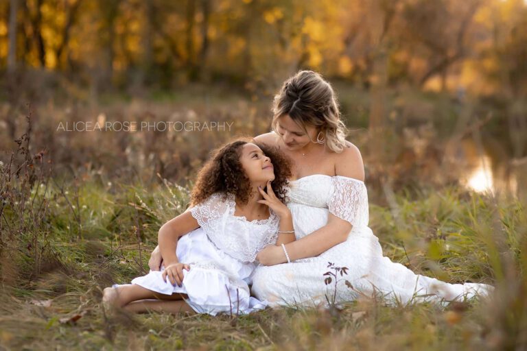 golden hour pregnant mom and older daughter sitting together in field in plymouth mn