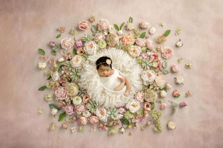 newborn girl in white surrounded by pink flowers