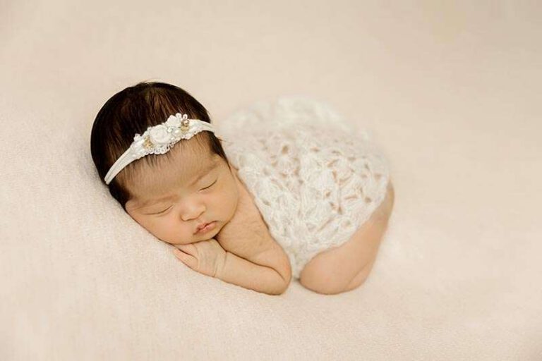 baby girl sleeping posed on pink background and white lace wrap