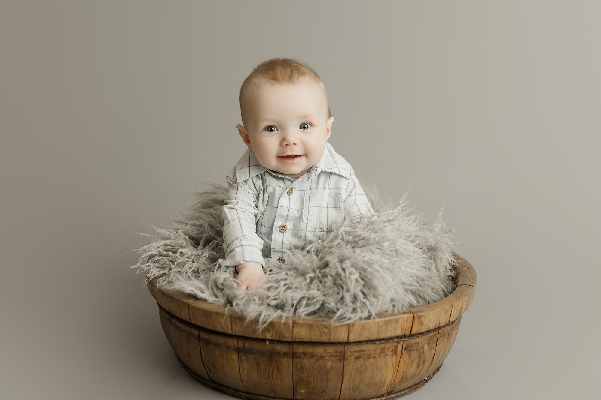 6 month old baby boy sitting in wood bowl on grey background