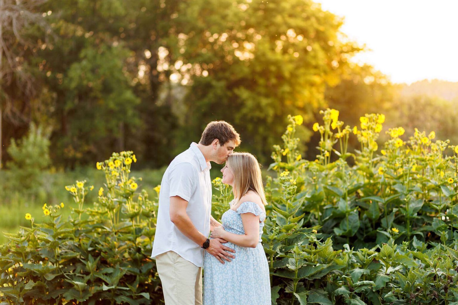 pregnant couple standing in field with sun setting behind them in minneapolis mn