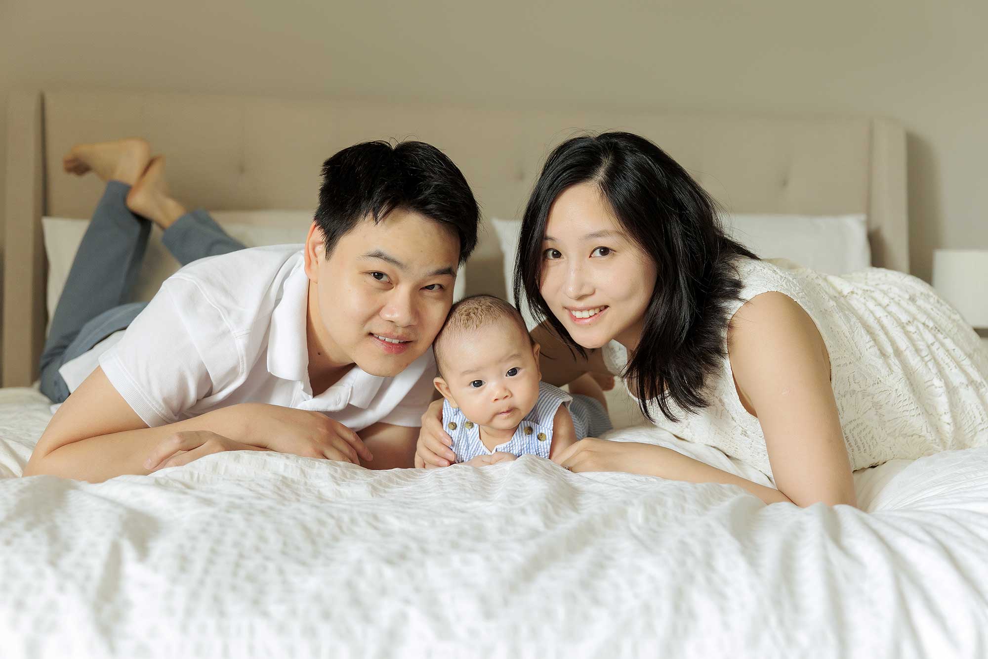 mom, dad, and 3 month old baby boy posing on bed together