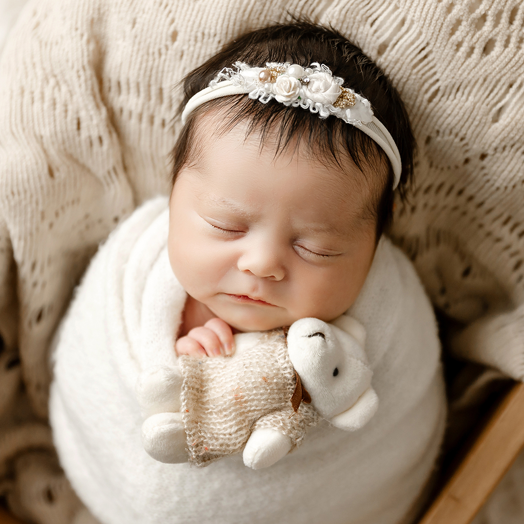 newborn girl wrapped in cream with matching headband holding bear in minneapolis studio