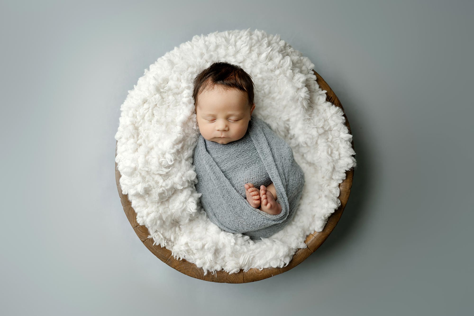sleeping newborn boy wrapped in blue in brown bowl in minneapolis baby photography studio