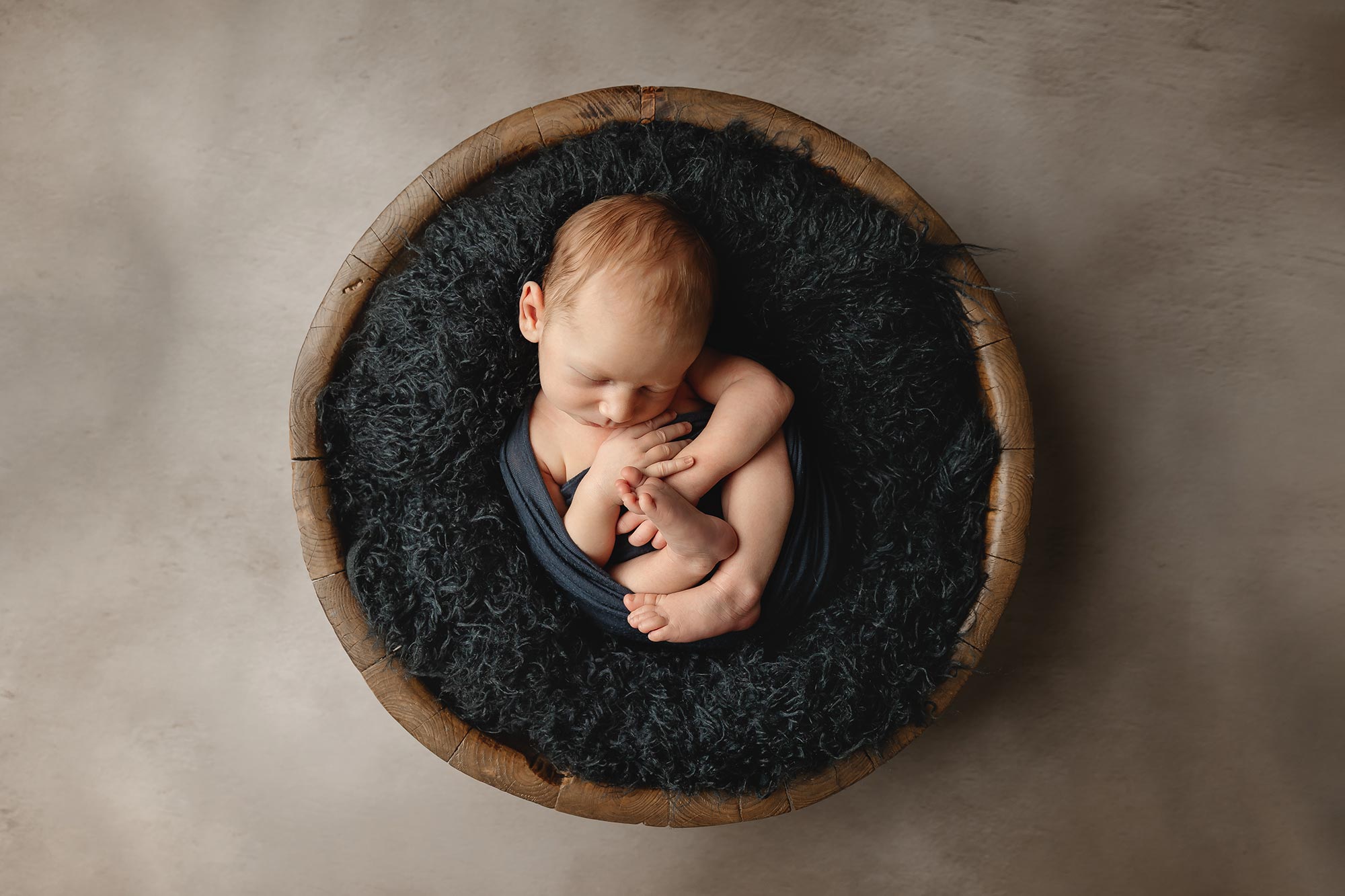 newborn boy wrapped in navy blue in brown bowl in newborn photography studio in twin cities