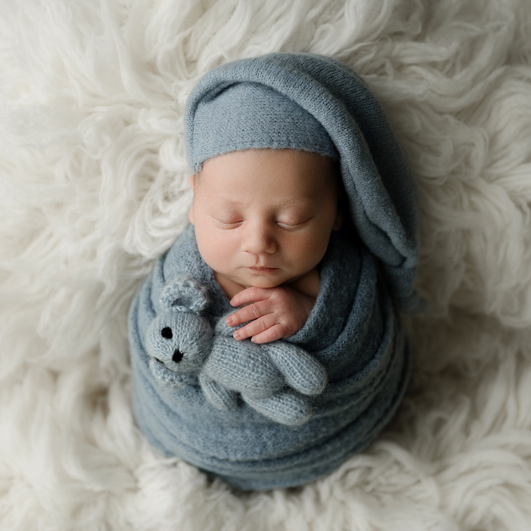 newborn boy wrapped in blue wrap holding bear