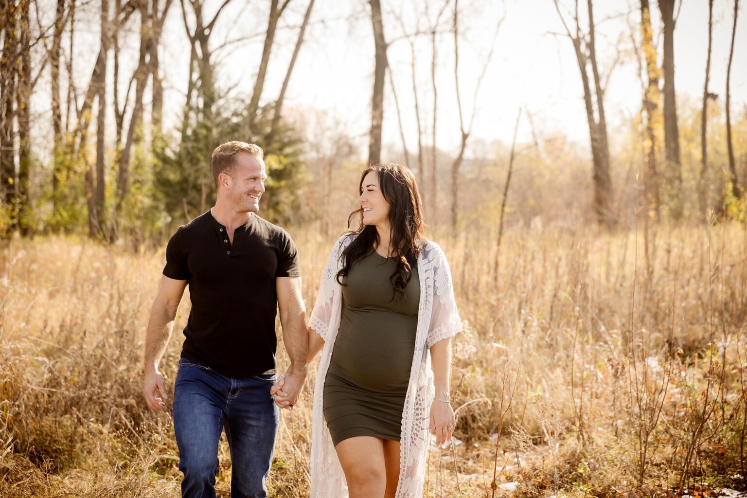 expecting couple walking through field in the twin cities