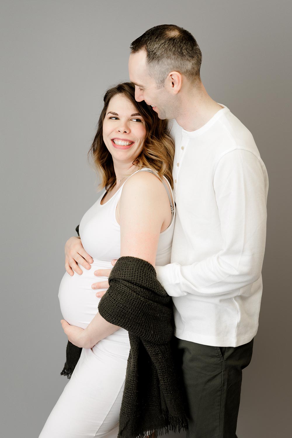 expecting couple in white and hunter green posing in twin cities portrait studio