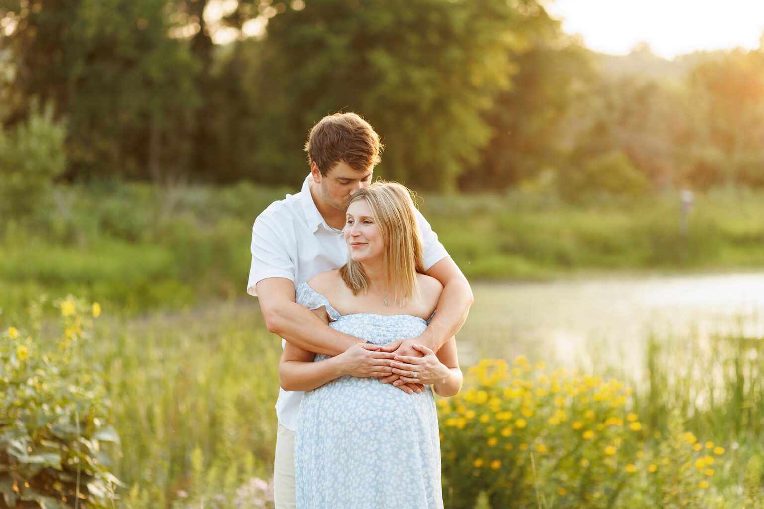 pregnant couple posing in field against setting sun in minneapolis mn
