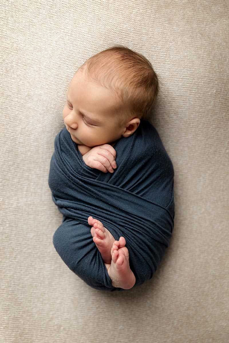 newborn boy wrapped in navy blue on tan blanket in minneapolis