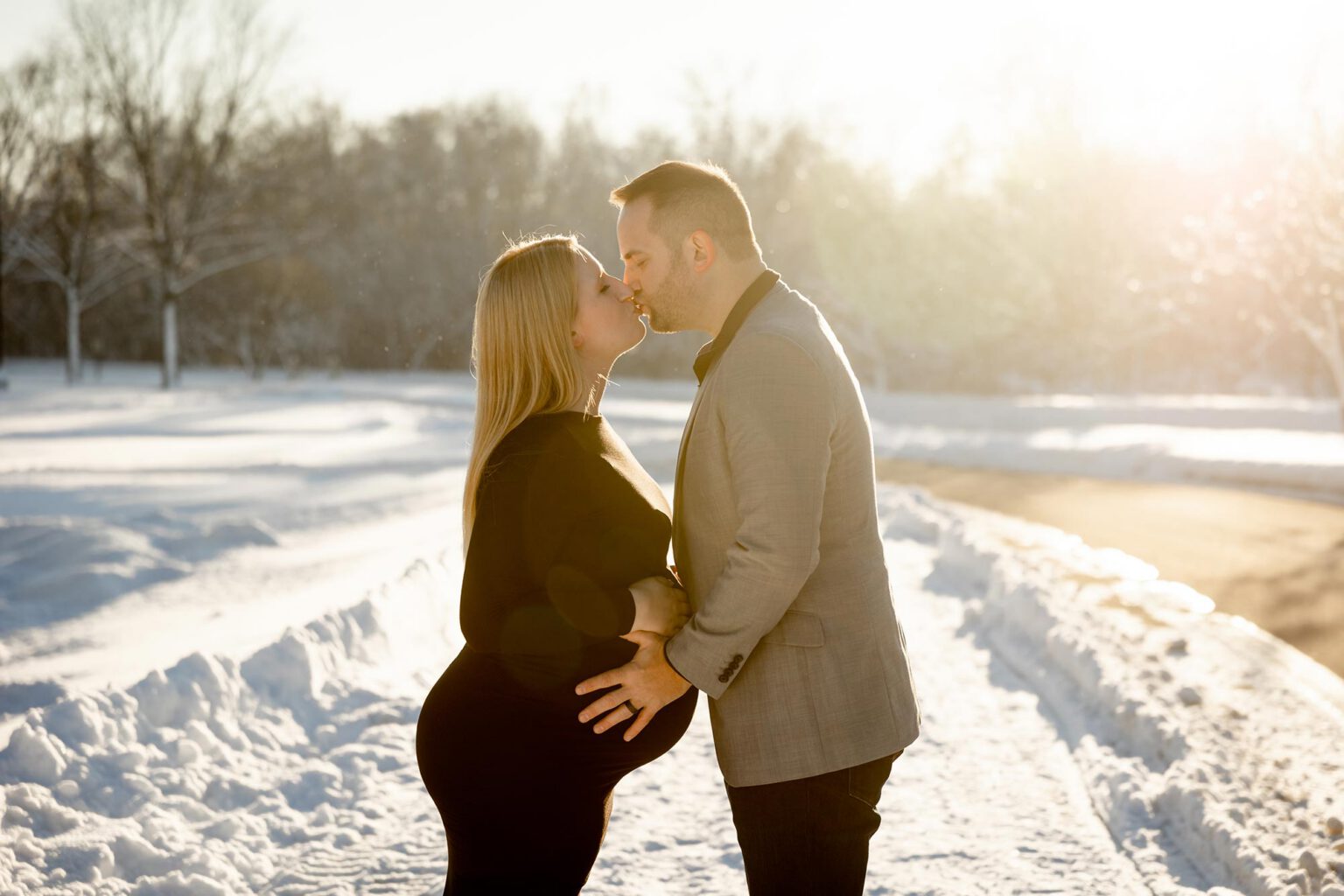 expecting couple standing in the snow kissing against a sunset in minneapolis mn