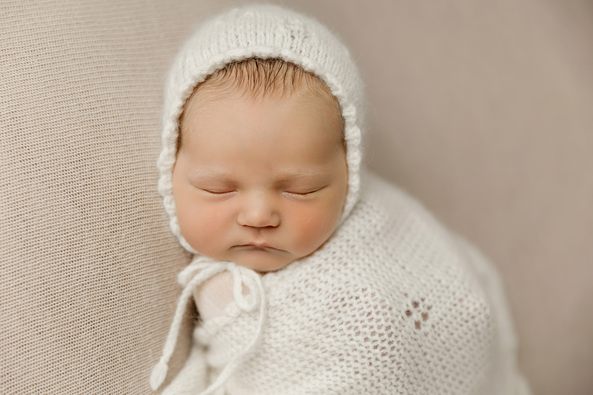 newborn girl sleeping in white wrap wearing matching bonnet