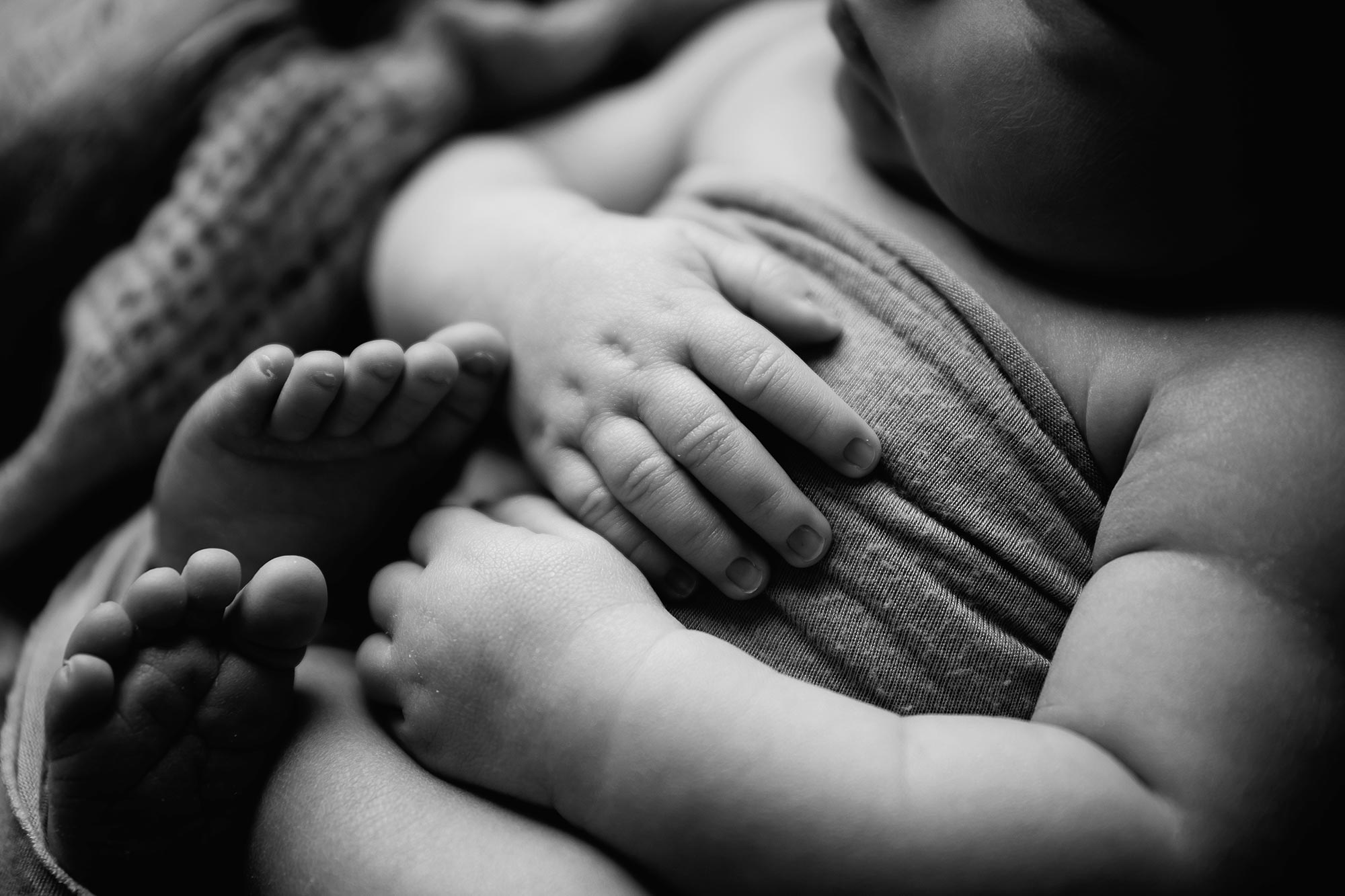 black and white macro shot of infants hand resting on belly in minneapolis newborn photography studio