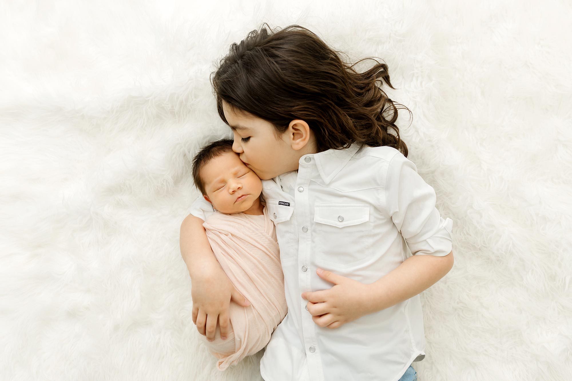 older brother lying with newborn sister on white rug at plymouth portrait studio