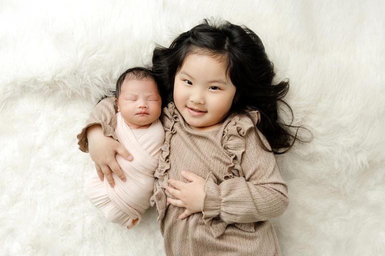 older sibling lying with newborn on white rug at minneapolis newborn studio
