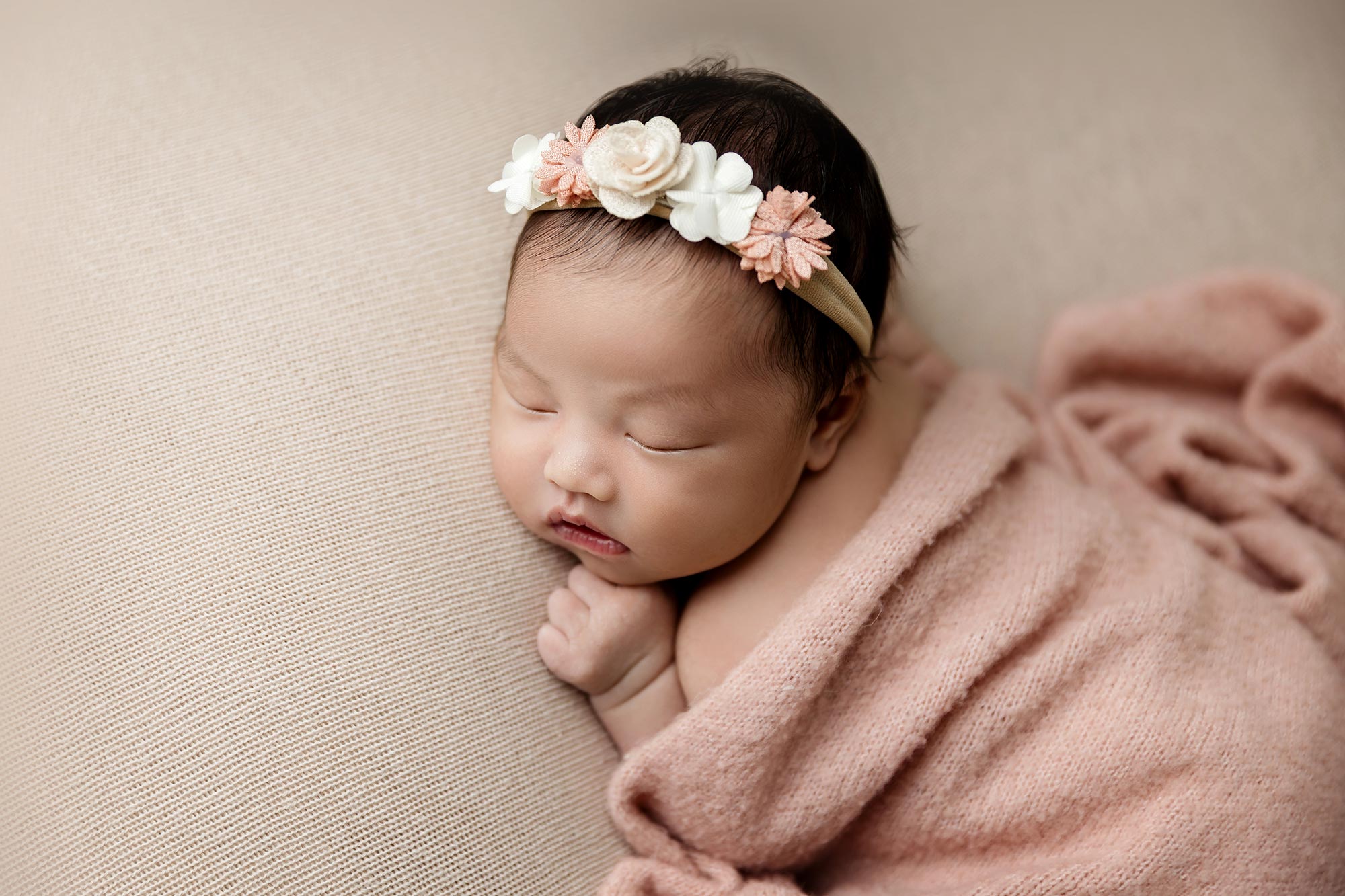 sleeping newborn girl wrapped in pink with flower headband at minneapolis studio