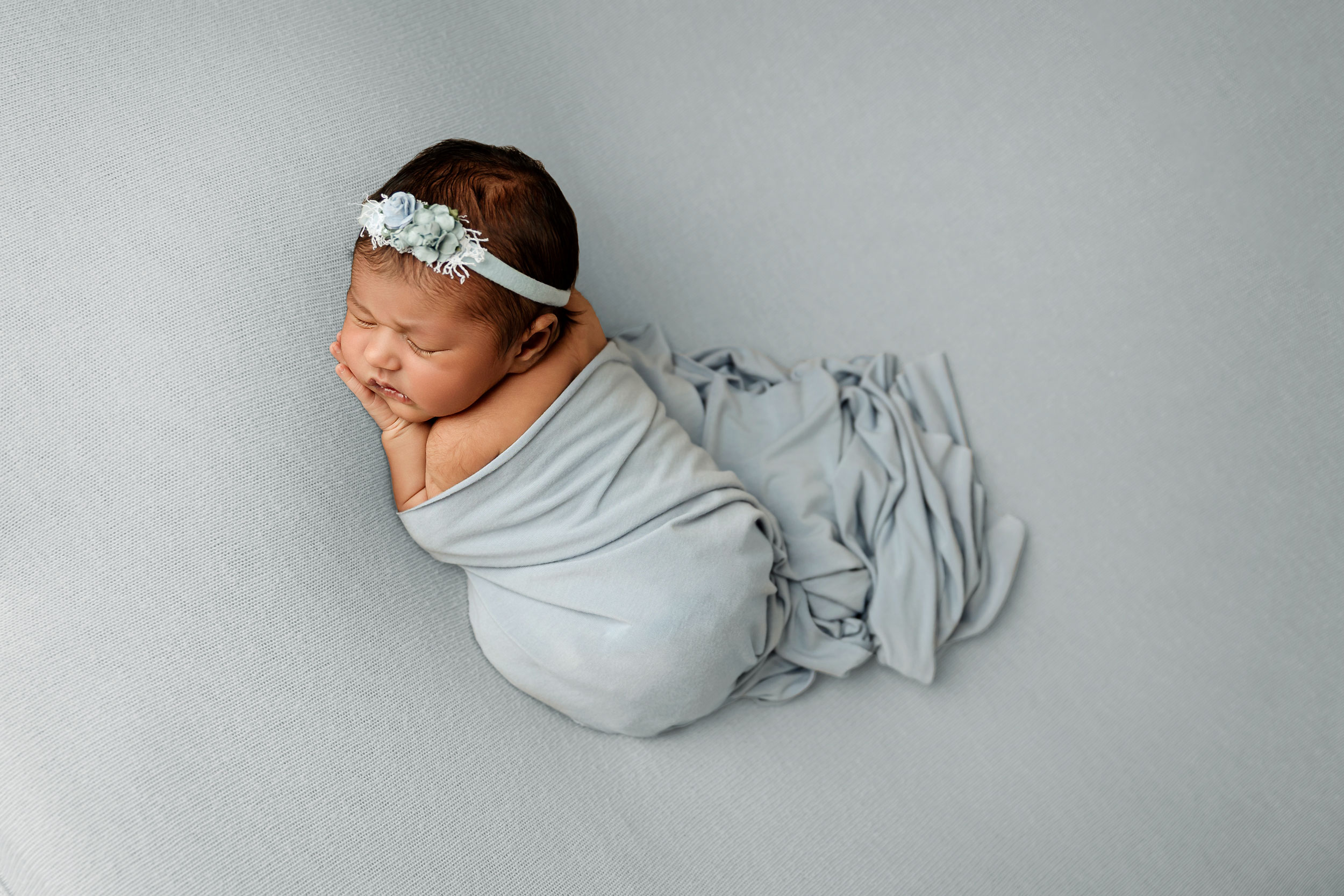 newborn baby girl wrapped in blue on blue backdrop at minneapolis newborn photography studio